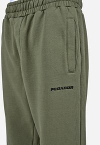 Olivové tepláky s rebrovaným pásom, bočnými vreckami a vystúpeným čiernym logom "PEGADOR" na stehne. Mäkká, textúrovaná tkanina.