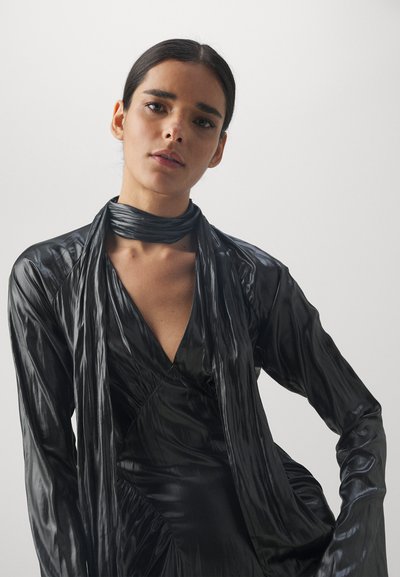 Robe noire, brillante, à manches longues avec un décolleté en V profond et un devant drapé. Comprend une écharpe assortie nouée autour du cou. Texture lisse.