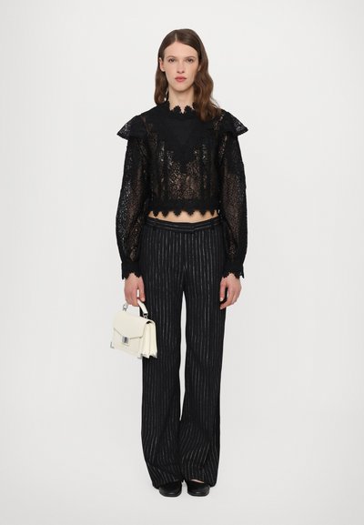 Black lace cropped long-sleeve top with ruffled shoulders, paired with black striped wide-leg trousers. Beige handbag with a silver clasp.