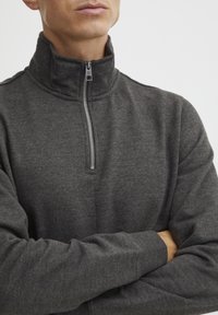Maglione grigio con zip, dotato di un colletto alto, realizzato in un tessuto morbido, con una breve cerniera metallica e polsini a costine. Texture liscia su tutta la superfice.