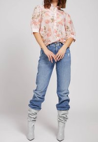 Bloemenblouse met knopen in lichtroze met groene accenten, gecombineerd met blauwe distressed jeans en grijze slouchy enkellaarsjes.