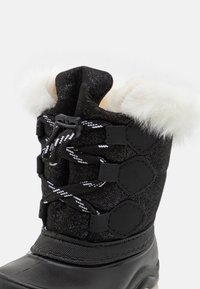 Czarne zimowe buty z teksturowaną cholewką z brokatem, białym futerkiem typu faux na kołnierzu, czarno-białymi sznurówkami i gumową podeszwą.