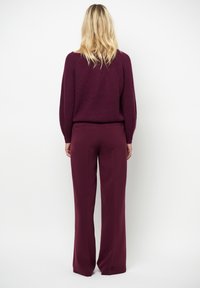 Bordeaux gebreide trui met raglanmouwen, gecombineerd met bijpassende wijde broek, beide met een gladde textuur en minimale details.