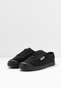 Sneakers neri in tela con punte in gomma, suole testurizzate e lacci per la chiusura. Presentano un'etichetta laterale con il nome del marchio.