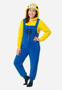 Tuta in peluche blu e gialla con zip frontale, cappuccio con due occhi e dettagli neri. Presenta un logo sulla parte anteriore e caviglie con polsini.