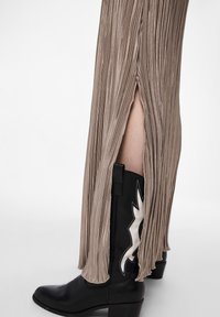 Bottes de cowboy noires avec un motif d'éclair blanc, associées à une robe maxi plissée beige avec une fente latérale et un tissu texturé.