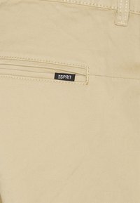 I pantaloni di cotone beige presentano una tasca posteriore con un'etichetta nera Esprit. Il tessuto ha una consistenza liscia e una sottile trama diagonale.