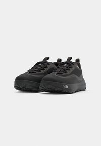 Zapatos exteriores negros con parte superior sintética texturizada, suela de goma pronunciada y un sistema de cordones minimalista. Presenta una marca en el talón.
