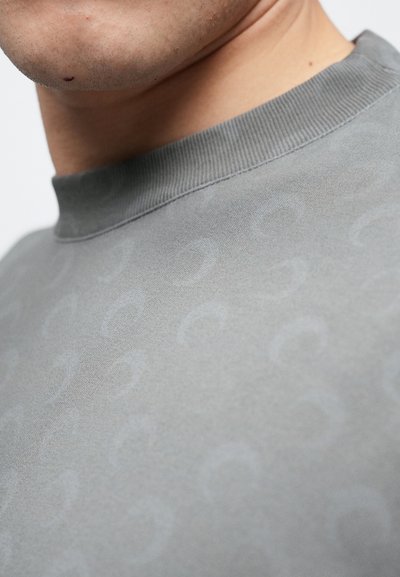 Szara bluza z zaokrąglonym dekoltem typu crew neck, z subtelnym zakrzywionym wzorem, prążkowanym kołnierzem i miękką fakturą. Skupienie na wykończeniu dekoltu i detalu materiału.