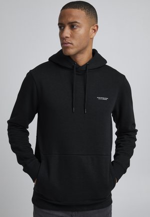 Sweatshirt à capuche noire en tissu doux, doté d'une poche kangourou à l'avant, de cordons de serrage et d'un petit logo sur la poitrine.
