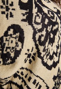 Tessuto beige con motivi astratti neri, caratterizzato da una trama morbida e testurizzata e fibre visibili, creando un effetto visivo dinamico.