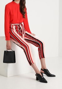 Röd långärmad skjorta med knappar, kombinerad med rosa och svarta randiga cropped-byxor, accentuerade med ett knytbälte; svarta blockklackskor och handväska.