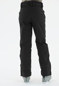 Zwarte waterdichte skibroek met een recht model, subtiele tailleband en ritsen bij de enkels. Draagt over grijze skibotten.