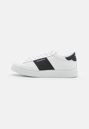 Sneakers bianchi in pelle con accenti neri e logo, dotati di suola piatta in gomma, punta rotonda e chiusura con lacci.