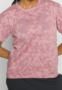 Krátký rukáv tričko v světle růžové barvě, s jemnou mramorovou texturou a velkým, bledým logem na přední straně. Vyrobeno z měkkého, elastického materiálu.