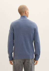 Svetlo modra rebrasta pulover z visokim ovratnikom in dolgimi rokavi, izdelan iz strukturiranega pletenega materiala, v kombinaciji s sivo denim jeans.