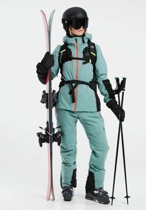 Das Skiausrüstungsset umfasst eine türkisfarbene Jacke mit schwarzen Akzenten, passende Hosen, schwarze Handschuhe, einen Helm, Skier mit pinken Kanten und Skistöcke.
