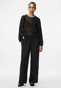 Melna mežģīņu apģērba komplekts ar caurspīdīgu, garām piedurknēm topu ar ziedu rakstiem un atbilstošas brīvas bikses, abiem ar teksturētu apdari.