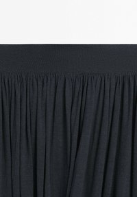 Black gathered fabric with wide elastic waistband, creating a pleated texture below the waistband.