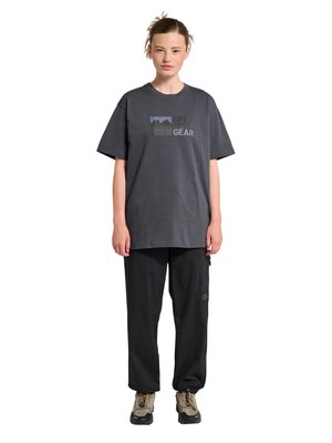 Kobieta ubrana w luźny ciemnoszary T-shirt z napisem "OFF GEAR", czarne spodnie typu cargo i beżowe buty turystyczne, stojąca na białym tle.