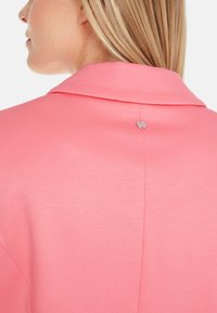 Pink collar shirt featuring a smooth texture, back button detail, and subtle stitching along the seams. Simple design with a professional look.
