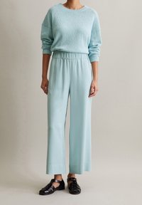 Vaaleansininen tekstuurinen neulepaita pyöreällä kaula-aukolla yhdistettynä leveälahkeisiin pehmeisiin housuihin, jotka ovat samaa sävyä, ja mustiin sandaaleihin.