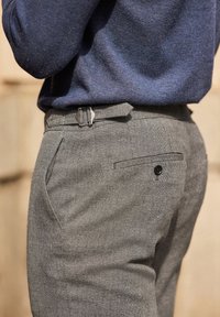Pantaloni grigi con texture e un sottile motivo a quadri, dotati di tasche laterali, una tasca a filetto con bottone e una cintura grigia coordinata.