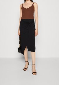 Brown tank top with decorative metal straps paired with a black knee-length wrap skirt featuring a twisted front and a side slit.