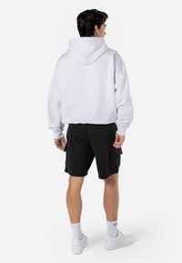 Hvid hoodie, blødt bomuldsstof, oversized pasform, kængurulomme, ribbede manchetter. Sorte shorts, cargo-stil, sidelommer, parret med hvide sneakers.