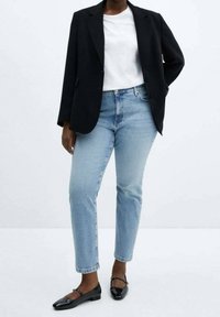 Blazer negro sobre una camiseta blanca, jeans de mezclilla azul claro y planos negros. El blazer tiene un corte entallado; los jeans son rectos con un ligero desgastado.