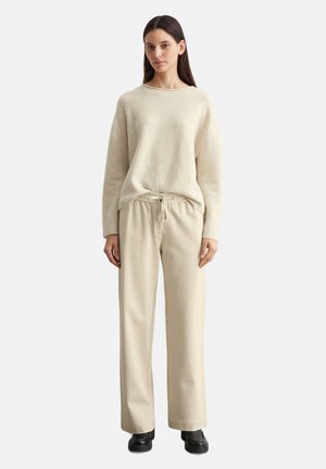 Beige gebreide trui met een ontspannen pasvorm, wijde mouwen; gecombineerd met beige joggingsbroek met trekkoord. Accessoires zijn zwarte enkellaarsjes.