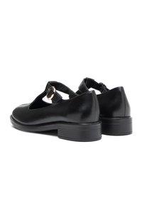 Een paar zwarte leren Mary Jane-schoenen met lage blokhakken en gouden gespjes, weergegeven vanuit een achteraanzicht op een witte achtergrond.