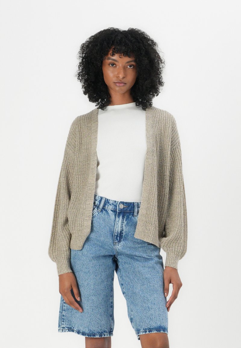 Beige gebreide cardigan met een losse pasvorm, geribde textuur, open voorkant en lange mouwen, gecombineerd met lichtblauwe denim shorts met hoge taille.