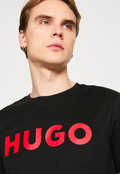 Черна тениска с яркочервен надпис "HUGO" отпред. Кръгло деколте, къси ръкави, памучен материал. Гладка текстура, удобен фит.