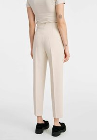 Beżowe spodnie o dopasowanym kroju i wysokim stanie, wykonane z gładkiego materiału. Charakteryzują się slim fit oraz detalami w postaci kantów po bokach.