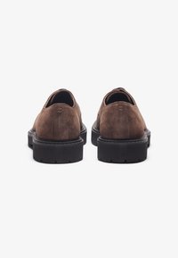 Scarpe in suede marrone con punta tondeggiante e una spessa suola in gomma nera. Presentano cuciture sottili e un tacco basso.