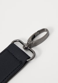 Sangle en cuir noir texturé avec un clip en métal. Le clip est de couleur argentée avec un loquet à ressort, solidement fixé à la sangle.