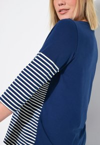 Laivastonsininen paita, jossa on raidalliset valkoiset ja laivastonsiniset hihat. Tässä on pyöreä pääntie ja rento istuvuus, ja se on valmistettu pehmeästä, kevyestä materiaalista.