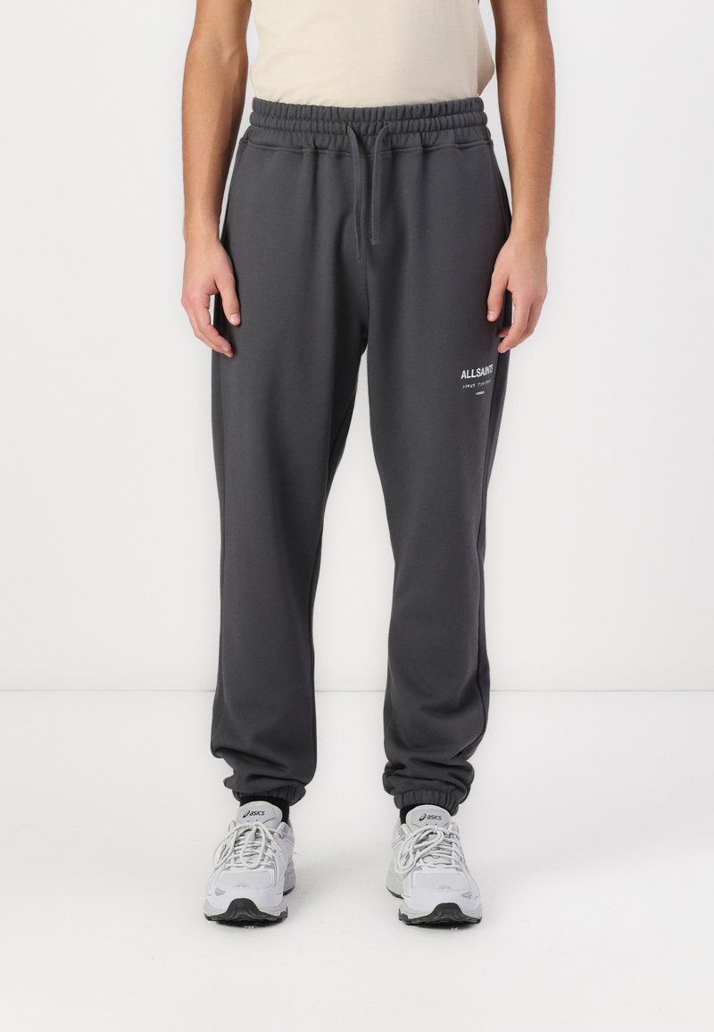 Kohlgraue Sweatpants mit elastischem Bund und Kordelzug, gerippten Bündchen und einem kleinen weißen Logo an der linken Oberschenkelseite.