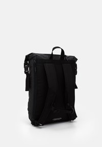 Černý batoh vyrobený z odolné tkaniny s nastavitelnými popruhy, horním madlem a prošívaným vzorem v horní části. Obsahuje zipy a akcenty.