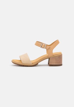 Beige lederen sandaal met een brede voorkantband, verstelbare enkelband en een gestapelde hak die op hout lijkt. Gestructureerde zool voor grip.