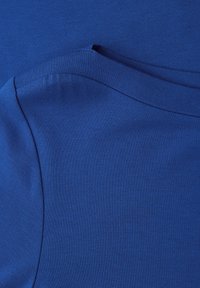 Blauer Stoff mit glatter Textur, ausgestattet mit einem runden Ausschnitt und geschwungenen Nahtdetails. Einheitliche Farbe ohne Muster oder Akzente.