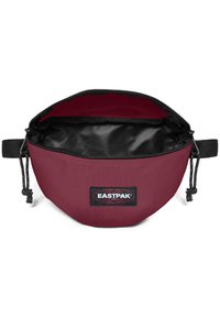 Eastpak-förvaringspåse i bordeauxfärgad tyg, rund form, dragkedjestängning, svart foder, varumärkespatch på sidan och snörningsaccent.