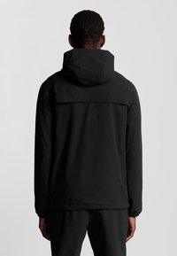 Veste noire légère avec capuche, en tissu uni, avec des poignets élastiques et un design épuré. Le dos présente une couture horizontale au niveau des épaules.