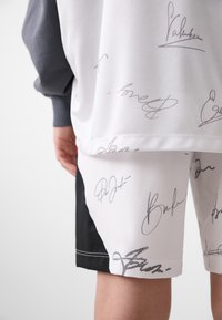 Short-sleeve gray sweatshirt and white shorts with black accents. Shorts feature black and gray signatures printed across the fabric.