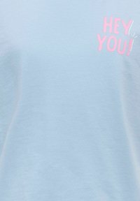 Tissu bleu clair avec texte rose "HEY YOU!" imprimé près du coin supérieur droit.