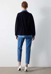 Tmavě modrá mikina s řaseným pasem, kombinovaná s džínovými kalhotami. Bílá lodičky dokončují outfit, který kombinuje ležérní i upravený vzhled.