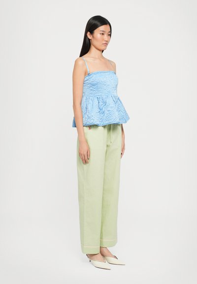 Top peplum de culoare albastru deschis, dintr-un material texturat, asortat cu pantaloni largi de culoare verde deschis și pantofi slip-on bej. Design simplu și curat.