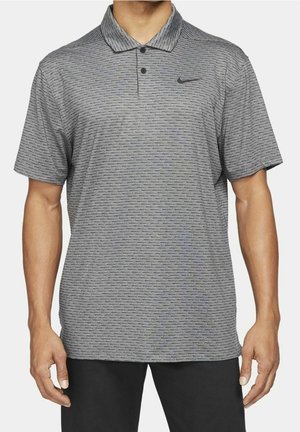 Homme portant un polo gris à manches courtes avec de fines rayures horizontales et un logo Nike sur la poitrine gauche, accompagné d’un pantalon noir.