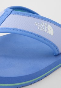Blå flip-flop med ett strukturerat ljusblått band, som har "The North Face"-logotypen i vitt. Mjuk skumgummisula med en grön accentrand.